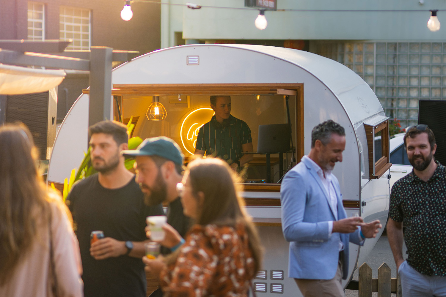 Guests enjoying live music at Caravan Sounds, a unique outdoor event featuring DJs performing from a vintage caravan in a vibrant social setting.